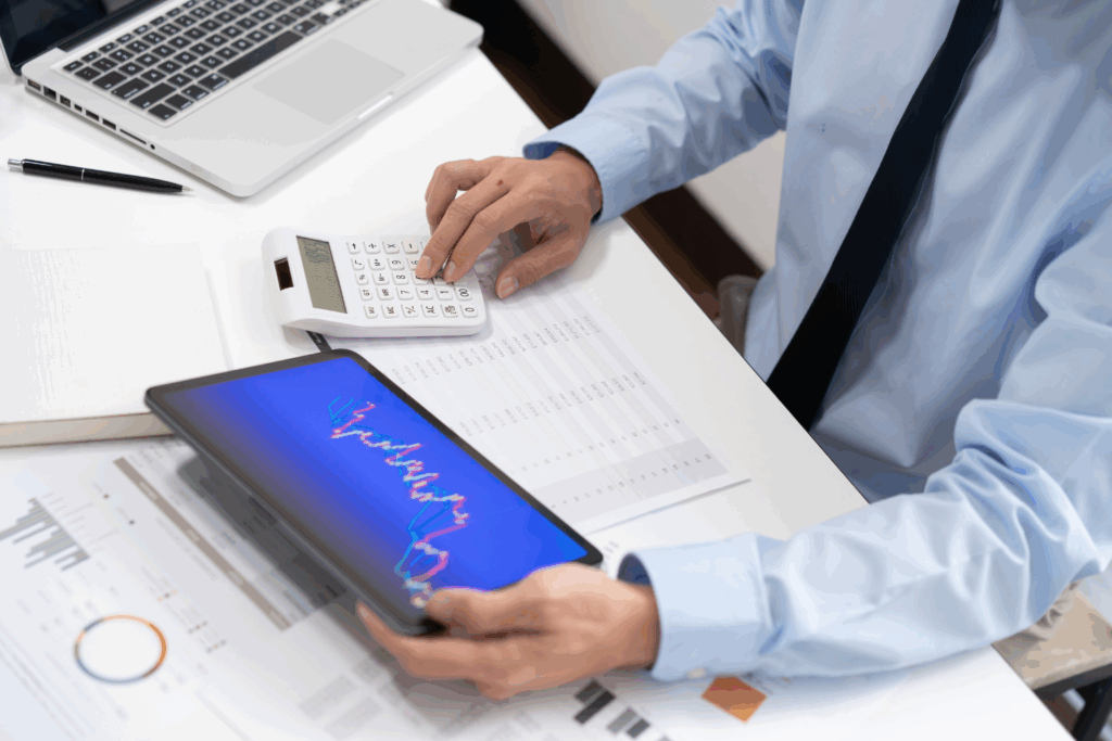 Pracownik analizujący raporty sprzedażowe i faktury w systemie ERP przy użyciu tabletu i kalkulatora.