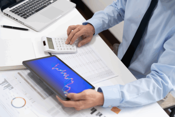 Pracownik analizujący raporty sprzedażowe i faktury w systemie ERP przy użyciu tabletu i kalkulatora.