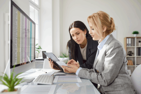 Dwie księgowe pracujące przy biurku z ekranem komputera pokazującym system ERP do automatyzacji procesów księgowych w firmie produkcyjnej.