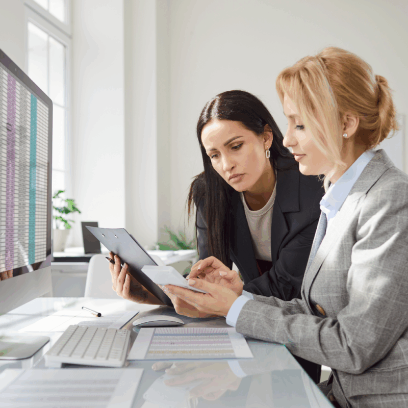 Dwie księgowe pracujące przy biurku z ekranem komputera pokazującym system ERP do automatyzacji procesów księgowych w firmie produkcyjnej.