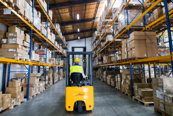 Wózek widłowy w alejce magazynu wysokiego składowania z regałami i kartonami